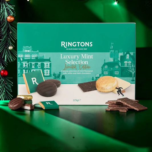 Ringtons Luxury Mint Selection Limited Edition chocolate box displayed on a green reflective surface with assorted chocolates and a biscuit in front, alongside a Christmas tree branch on the left.