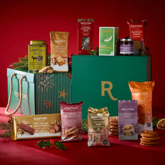 A Ringtons Christmas gift hamper filled with assorted tea, biscuits, and sweets, displayed alongside a large green branded box on a red background.