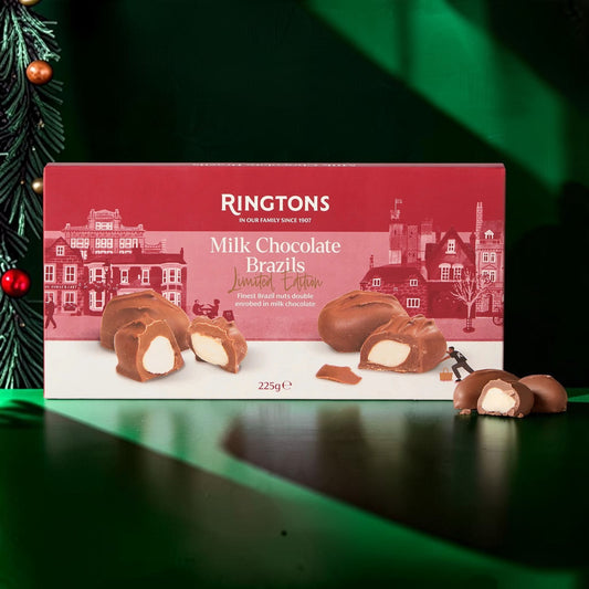 A box of Ringtons Milk Chocolate Brazils Limited Edition alongside several chocolate pieces, set against a festive green background with a pine branch on the left.