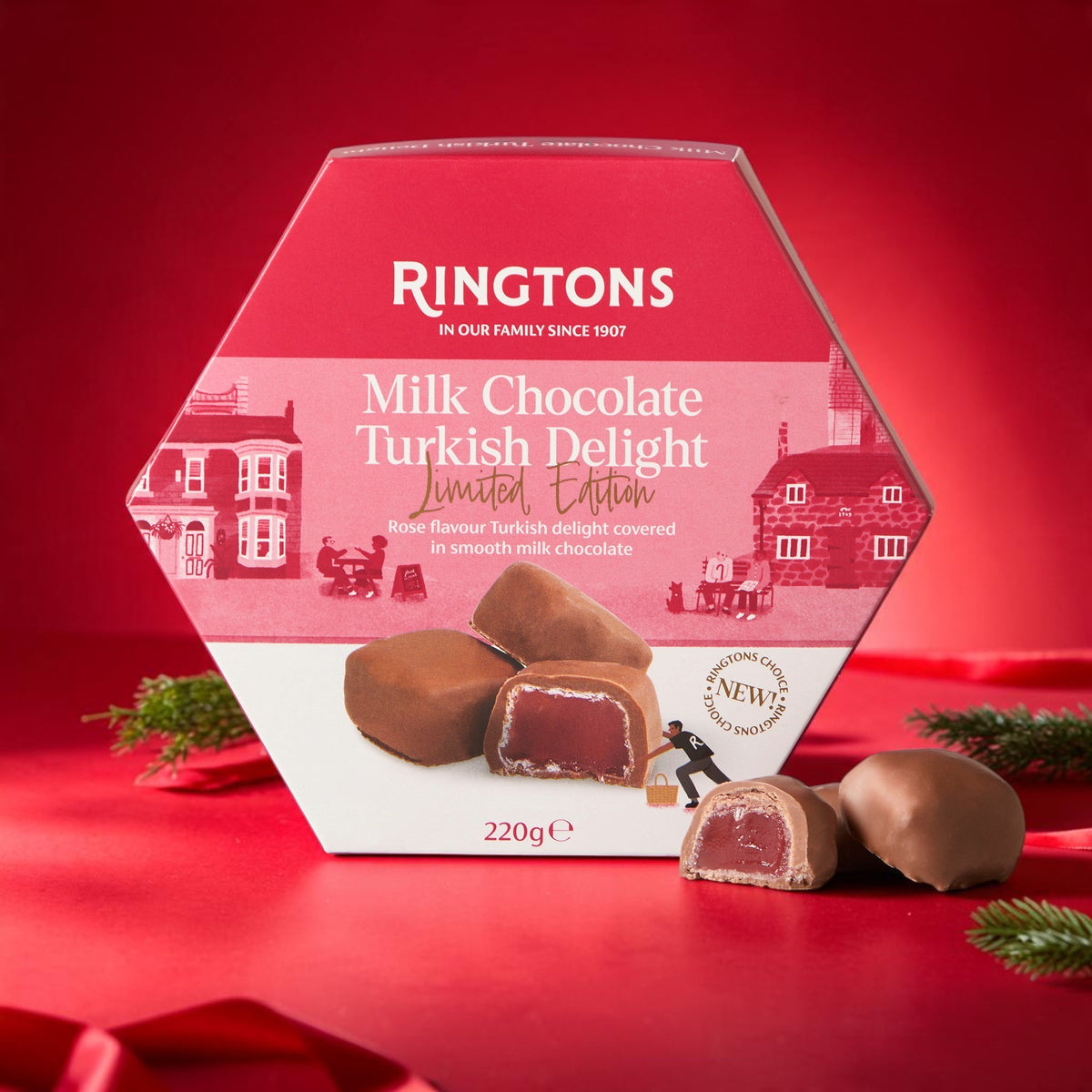 A hexagonal Ringtons Milk Chocolate Turkish Delight box in red and white, with two chocolate pieces displayed in front on a red surface against a red background.