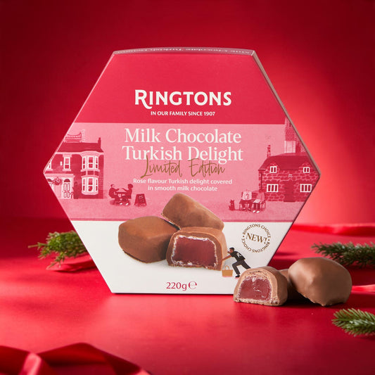 A hexagonal Ringtons Milk Chocolate Turkish Delight box in red and white, with two chocolate pieces displayed in front on a red surface against a red background.